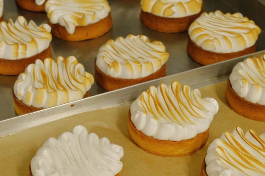 A baking tray of lemon meringue tarts with swirled, lightly toasted meringue topping, fresh from a Parisian patisserie