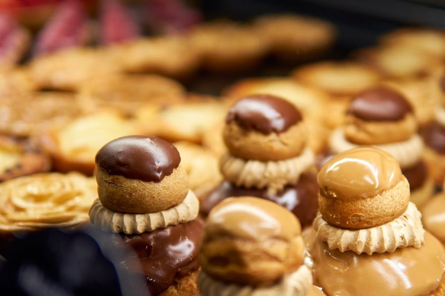 A display of religieuse pastries in a French bakery, each consisting of two choux buns stacked and glazed in chocolate or caramel