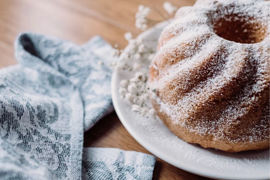 A ring-shaped kouglof dusted with icing sugar, placed on a white plate with a blue floral linen napkin alongside