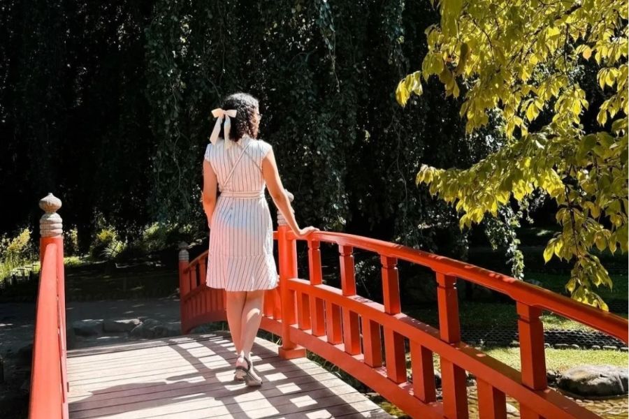 This is a lady walking over a bridge in a beautiful Japanese garden. She is facing away from the camera.