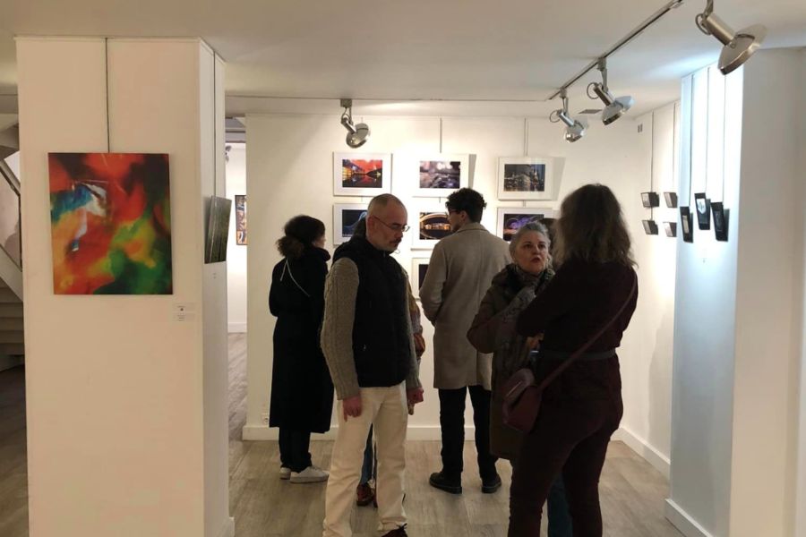 This is an image of a group of people standing around in small pairs looking at art and discussing.