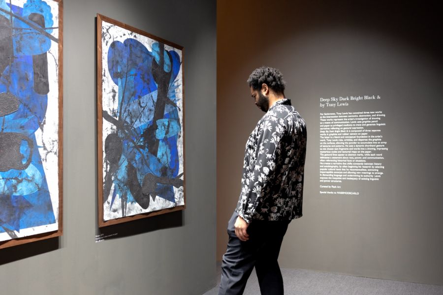 This is an image of a man standing in front of a blue painting looking at it and reading.