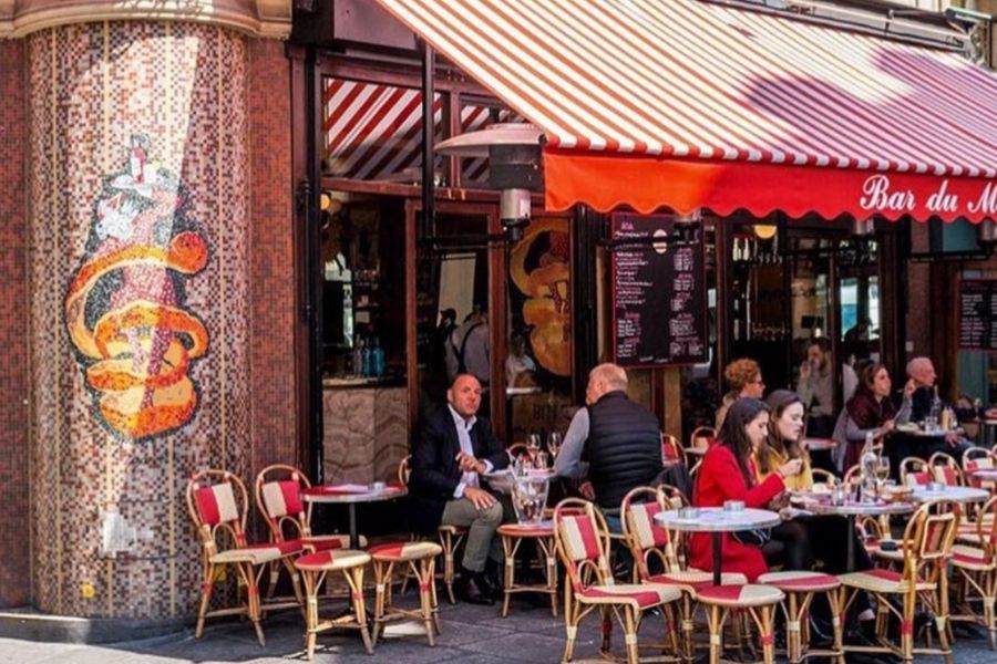 This is an image of a cafe with seating out the front and a red, striped blind to keep the sun out.