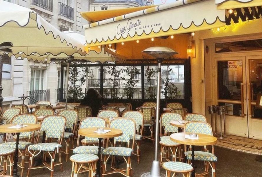 Best Non-Touristy Cafes in Paris: This is an image of a cafe with plenty of arranged seating out front and yellow blinds.