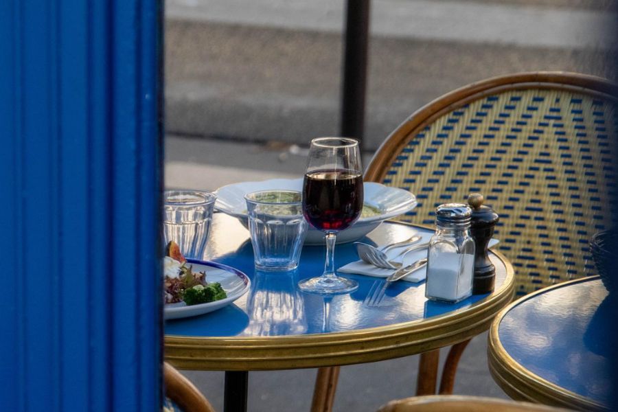 This is an image of a blue cafe table outside with wine and some plates of food on top.
