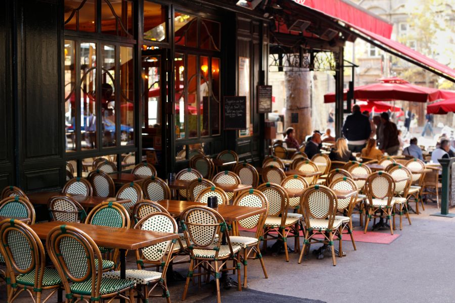 This is an image of the front exterior of a popular cafe with nice chairs and a red blind coming out to stop the sun getting on diners.