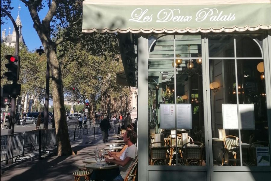 This is an image of the outside window of a lovely cafe in Paris with seating on the sidewalk around it.