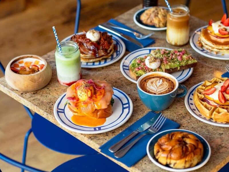 This is an image of a beautiful spread of breakfast dishes on a table with lattes and strawberry matcha.