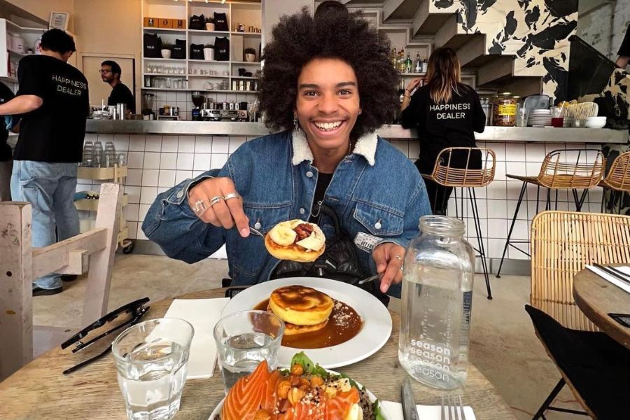 This is an image of a person smiling holding up pancakes in the middle of a café.