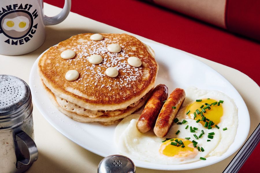 This is an image of a plate of American breakfast with pancakes, sausages and eggs.