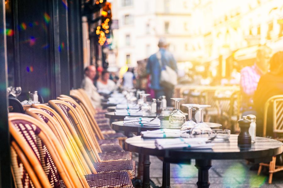 This is an image of cafe with tables out front, sporting glasses and cutlery.