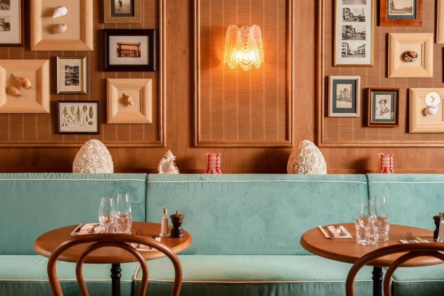 This is an image of a beautiful restaurant filled with art and mood lighting. The tables have glasses on them and cutlery.