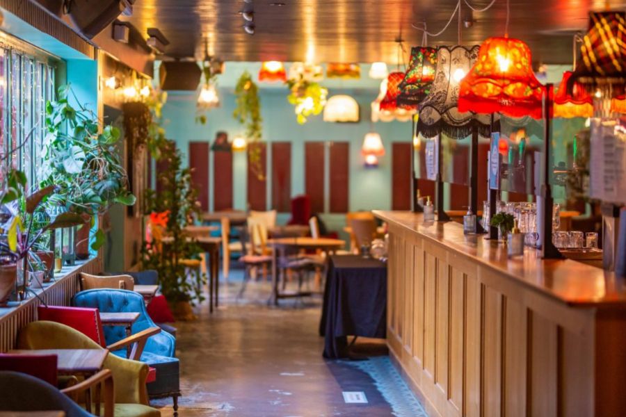 This is an image of a colourful bar full of bright furniture, plants and vintage lampshades.