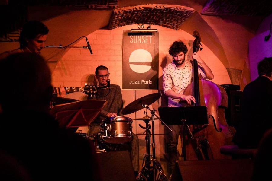 This is an image of a jazz band on a small stage with red lights shining down on them.