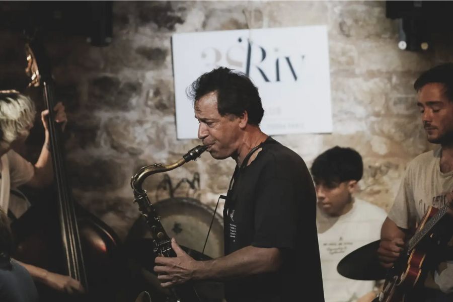 This is an image of a man blowing into a saxophone performing with his band mates on stage.