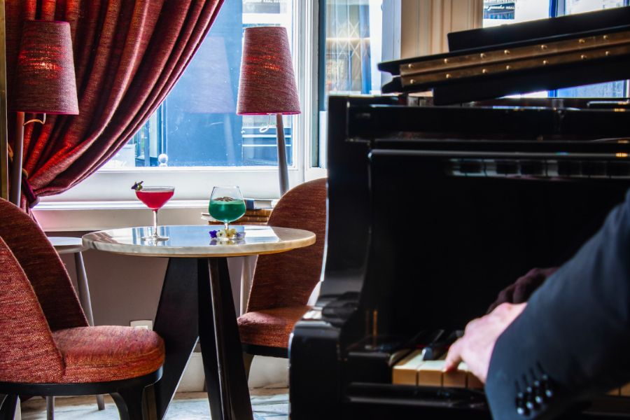 This is an image of a classy room with a grand piano and a table with cocktails on it in the background.