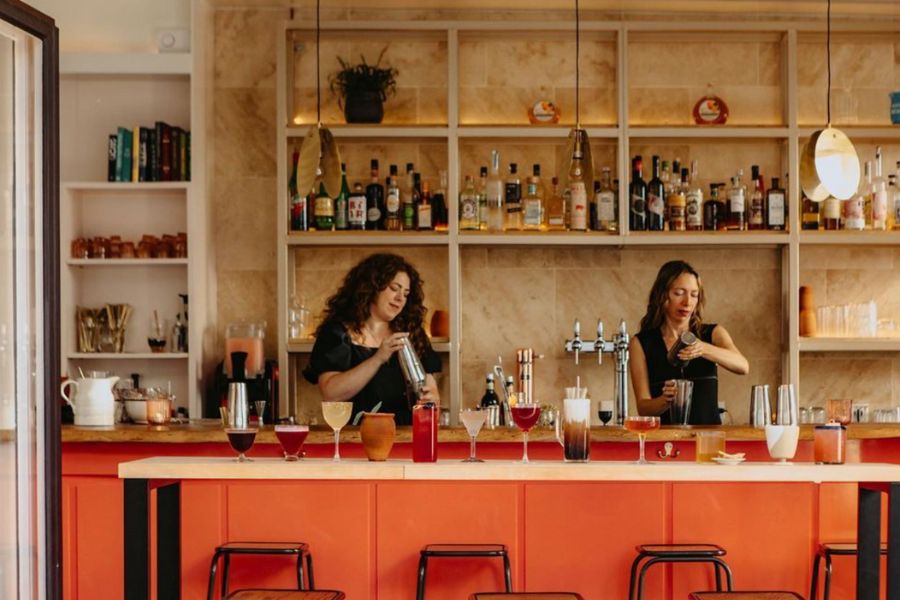 This is an image of two people shaking cocktails and serving drinks at an orange bar.