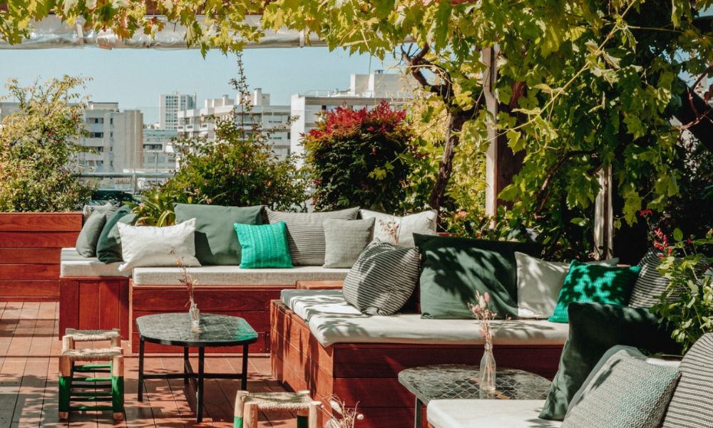 This is an image of an outdoor terrace with lots of wooden seating and cushions, plus greenery.