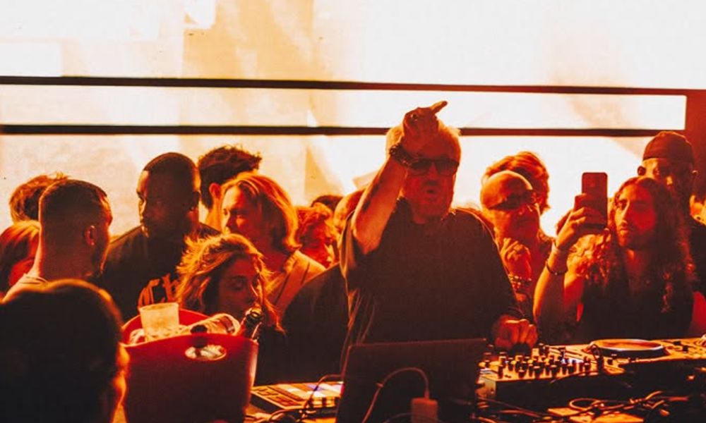 This is an image of a man on the DJ decks at a rooftop bar with plenty of people around dancing and chatting.
