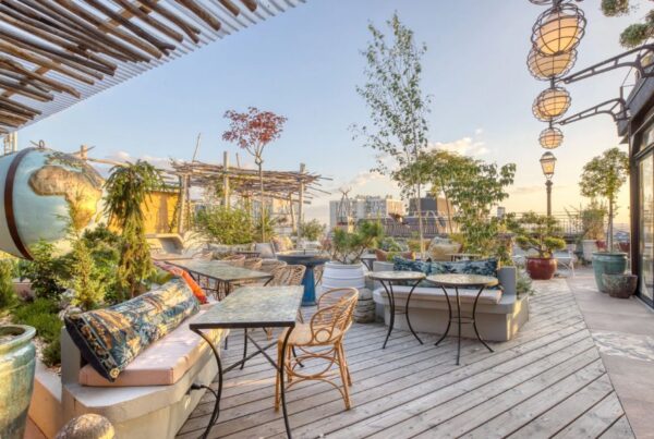 This is an image of a lovely deck full of boho furniture and mood lighting. The sky is also very blue and looks out on the Paris skyline.
