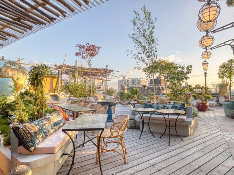 This is an image of a lovely deck full of boho furniture and mood lighting. The sky is also very blue and looks out on the Paris skyline.