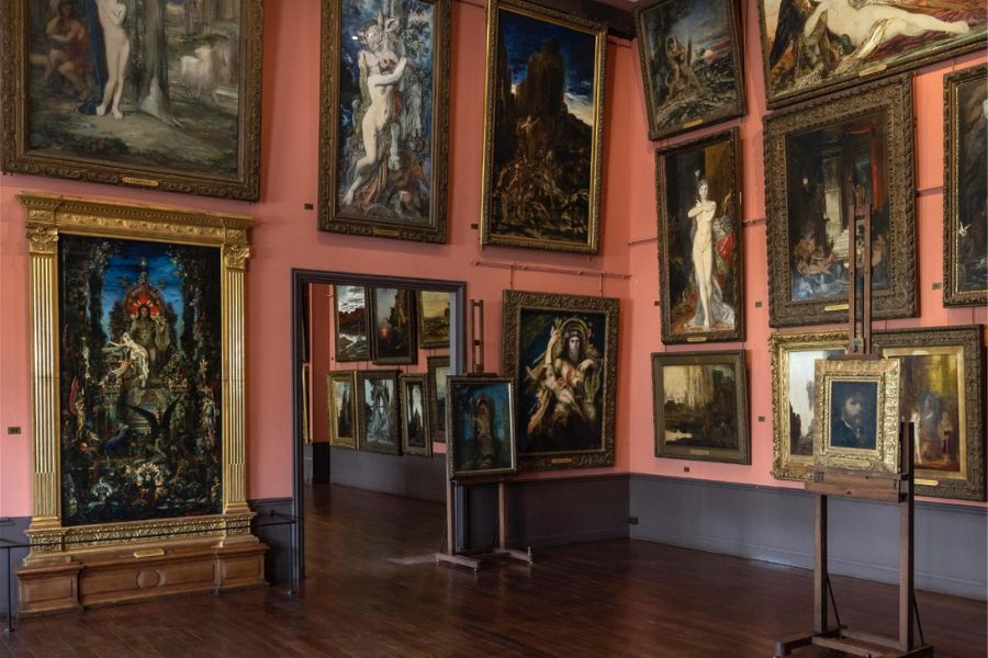 This is an image of an art exhibition room with beautiful paintings hung all around the ceilings and walls.