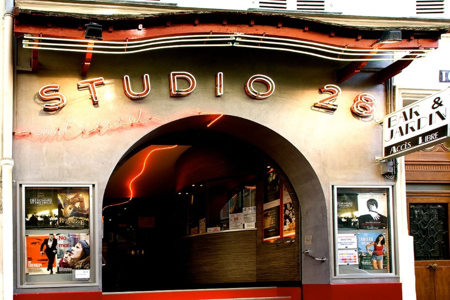 The neon-lit facade of Studio 28, a historic arthouse cinema in Montmartre, Paris A ornate vintage carousel with swing seats, decorated with painted cherubs and French flags, photographed from below against a blue sky