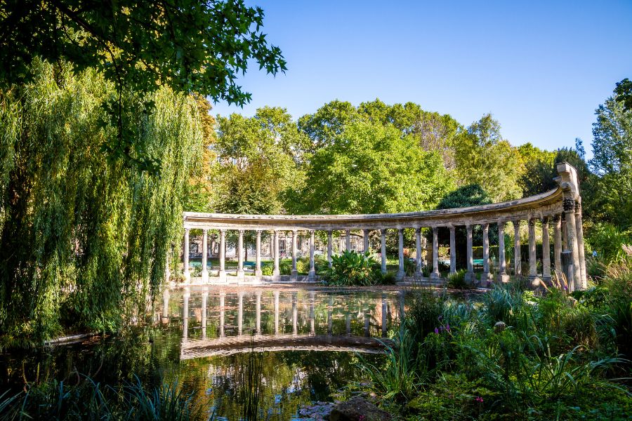 The curved Corinthian colonnade reflected in the lily pond at Parc Monceau, Paris, surrounded by weeping willows and lush greenery