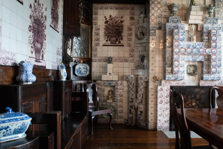 A room lined floor-to-ceiling with antique blue-and-white Delft tiles, featuring dark wood furniture and blue-and-white ceramic pieces