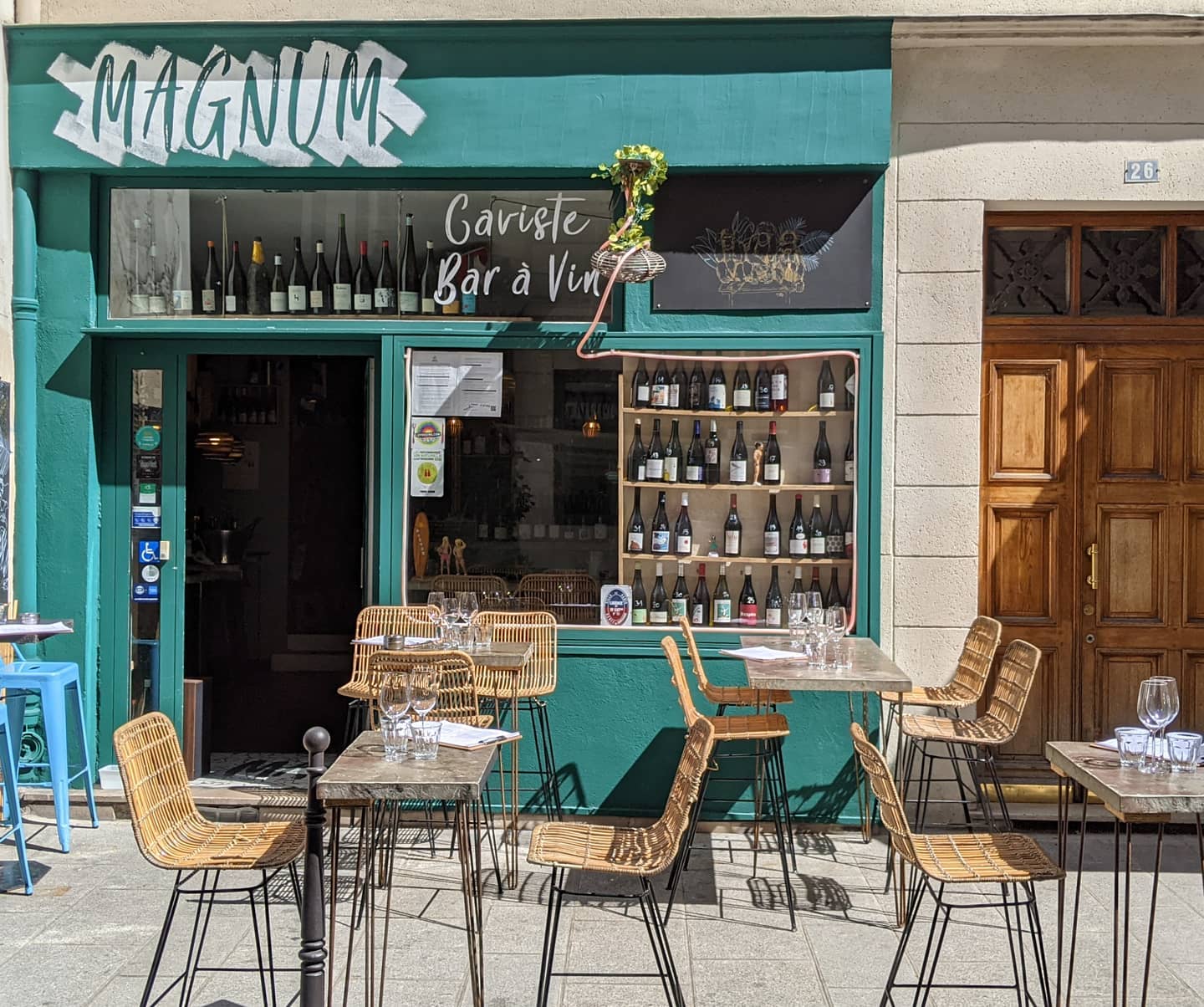 The green shop front of the wine bar, with tables and chairs outside.