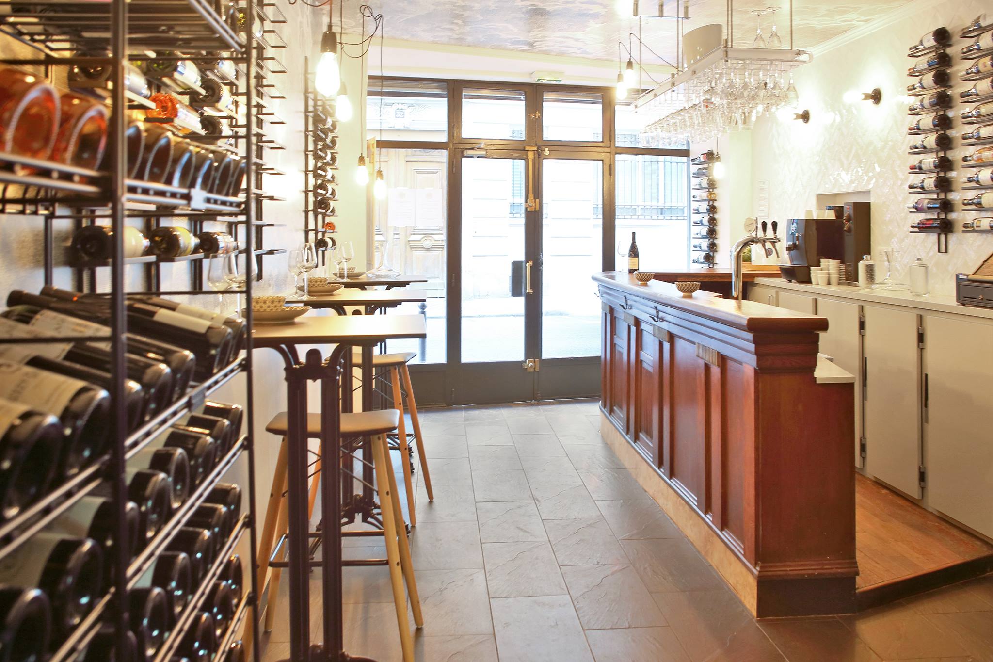 Inside a bright airy wine bar. One side of the room is a wooden bar, the other are shelves of wine.
