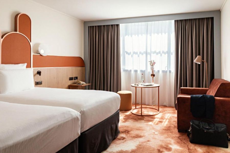 A twin hotel room in Paris with terracotta arch headboards, white bedding, a rust-coloured armchair and a patterned carpet