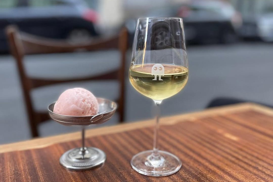 A metal dish with one single scoop of ice cream and one glass of white wine.
