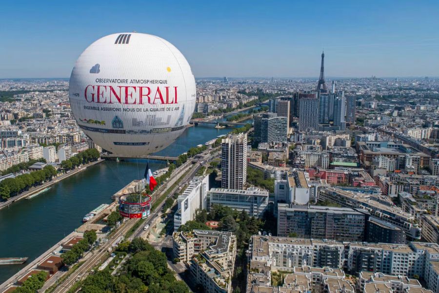 An aerial view of Paris showing the Generali tethered hot air balloon floating above the Seine, with the Eiffel Tower visible in the distance