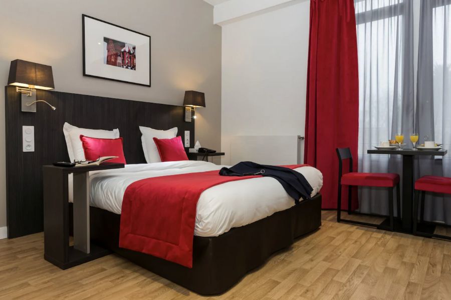 This is a lovely apart-hotel in the heart of Paris with a spacious bedroom, with a dining table and red bedding.