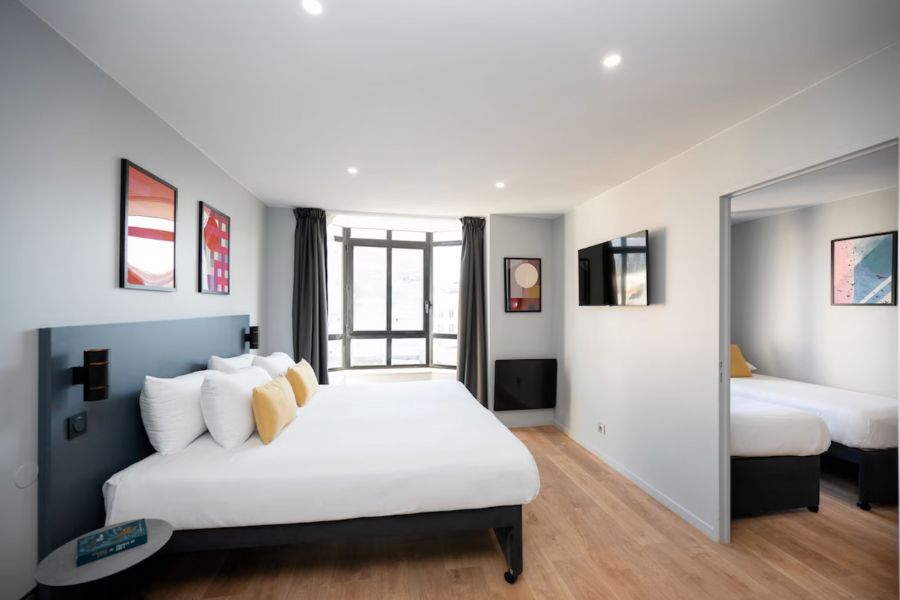 This is an image of the main bedroom in a Parisian apart-hotel. There is a double bed in the centre and white sheets on the bed.