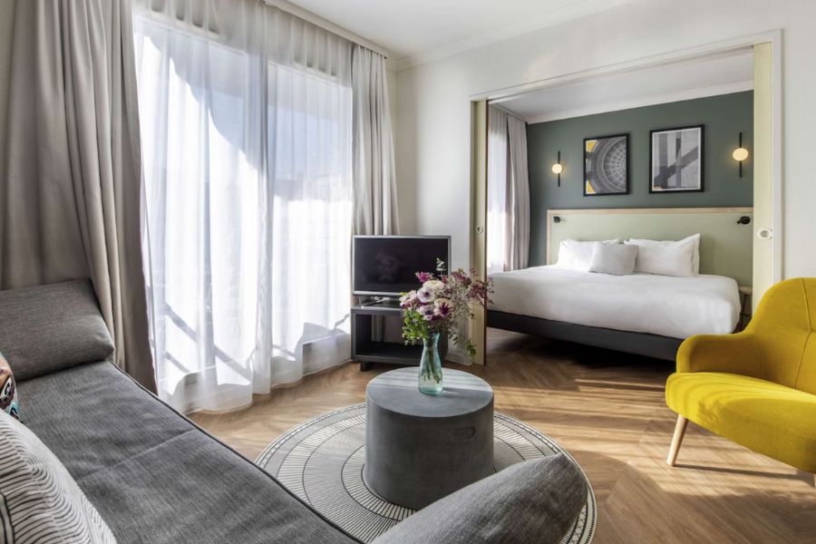 This is an image of a studio apart-hotel in Paris with a double bed and living room with couch and tables opposite.