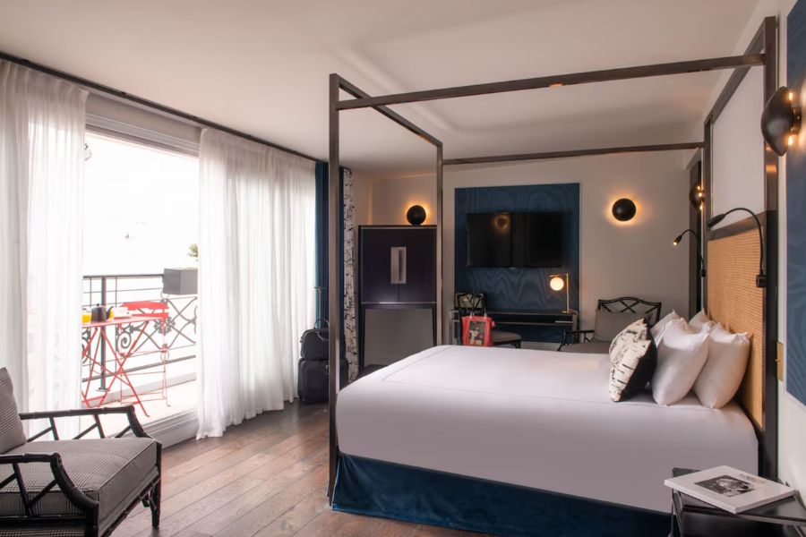 This is a picture of a Paris hotel room with a four poster bed and white minimalist sheets.