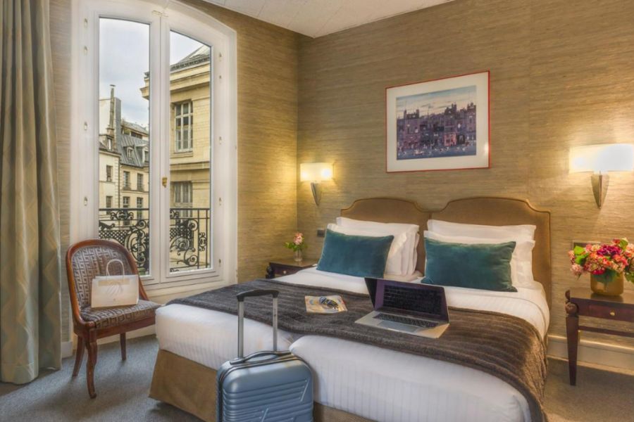 This is an image of a nice hotel room in Paris with a double bed and a great view of Parisian buildings.