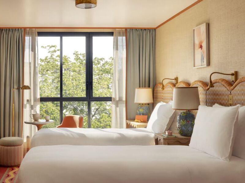 This is an image of a light, airy hotel room with two single beds and a big window.
