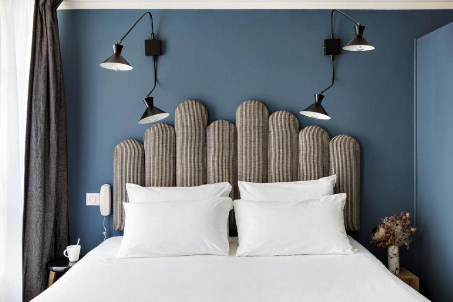 This is an image of a nice hotel room with a double bed with white linen, alongside a blue feature wall.