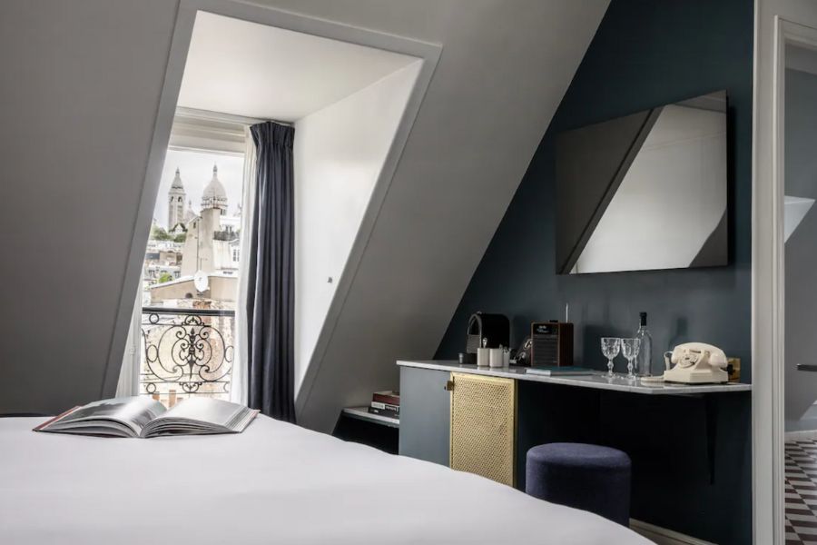 This is an image of a hotel room with a view of the Sacre Coeur Cathedral outside the window in the distance.