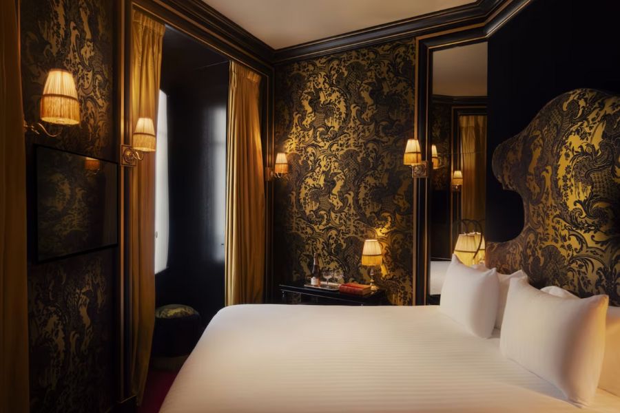This is an image of a very regal hotel room with a double bed and gold detailing on dark walls.