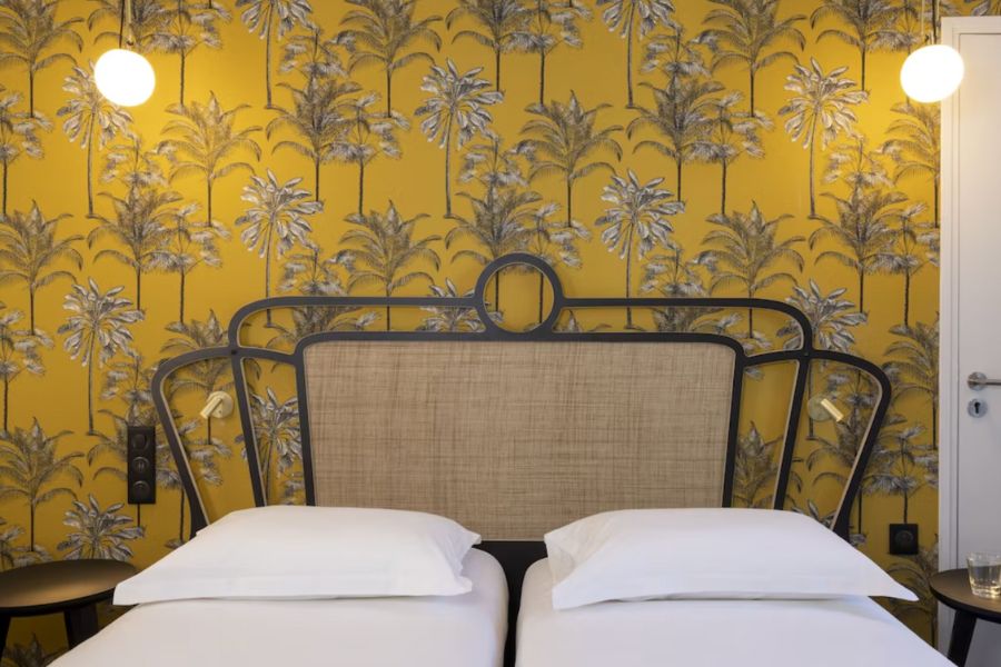 This is a minimalist hotel room in the Latin Quarter of Paris featuring a yellow feature wall, and a double bed with white bedding.