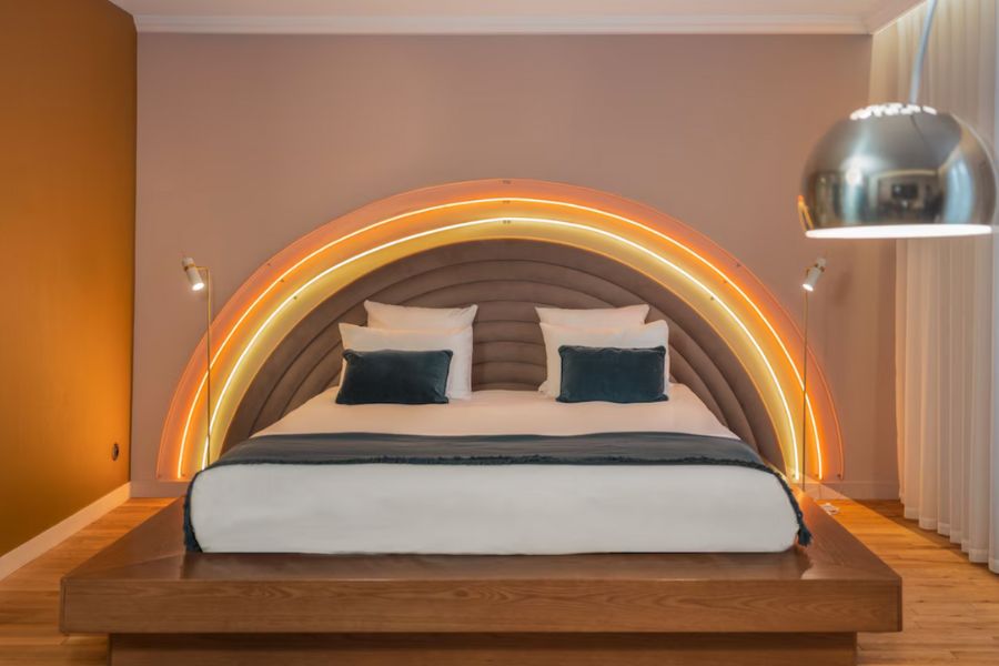 This is a cool, minimalist hotel room in the Latin Quarter of Paris featuring a rainbow, light-up head board and white bedding.