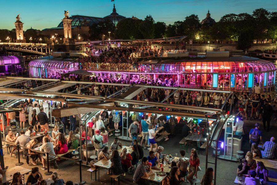 This is an image of a big bar on a boat along the Seine River. Lots of people are milling around.