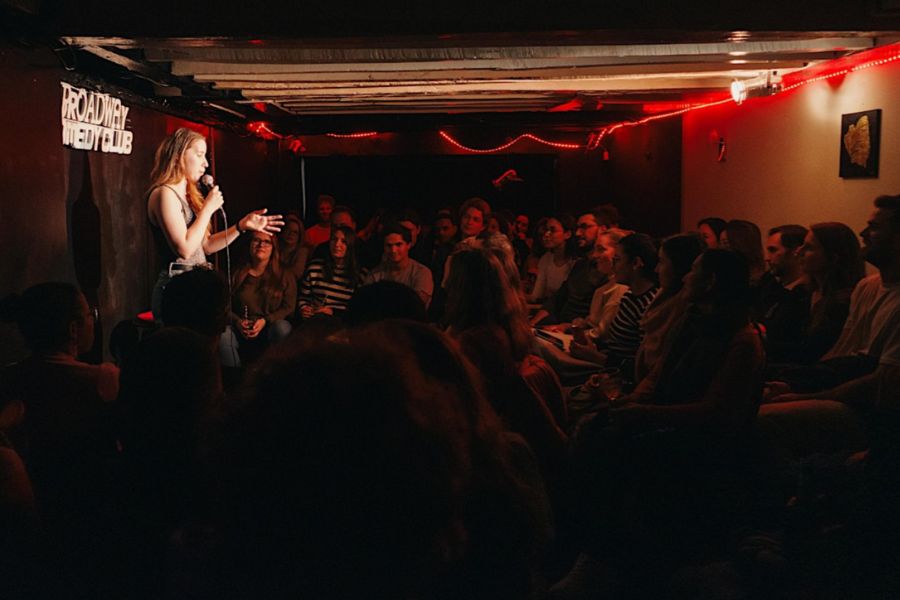 This is an image of a comedy club audience sitting around a comedian on stage with a mic.