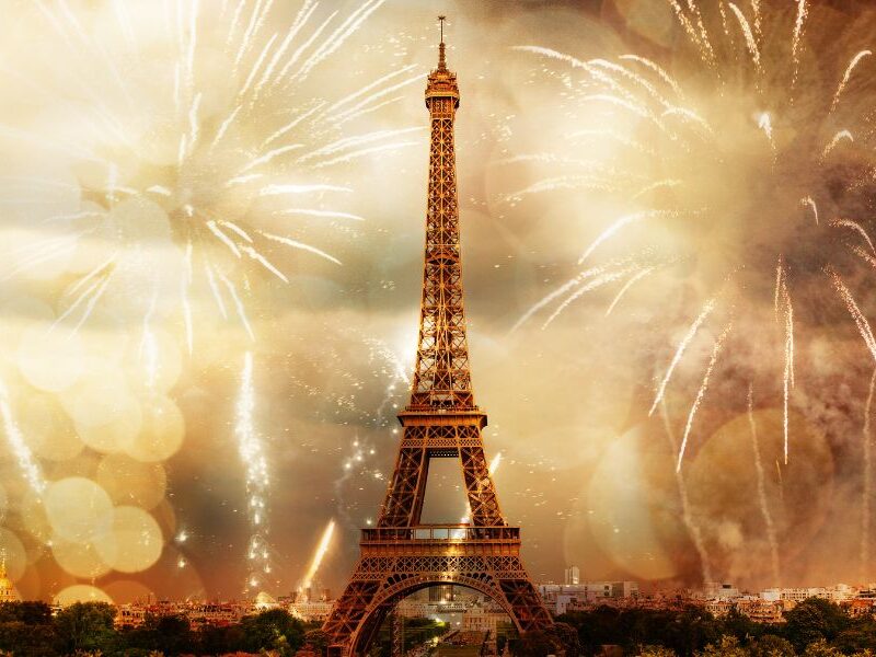 This is an image of the Eiffel Tower in the evening with fireworks all around it.