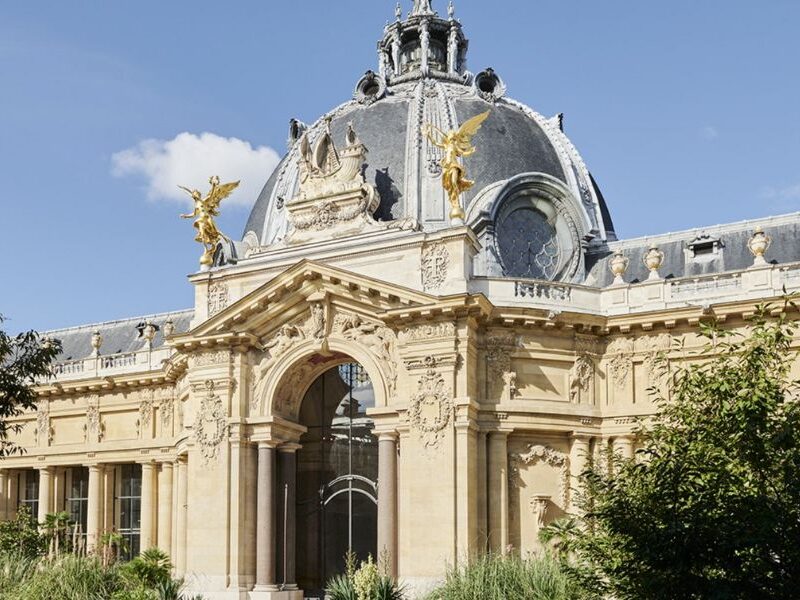 This is an image of a big building with regal gold detailing and greenery in front of it.