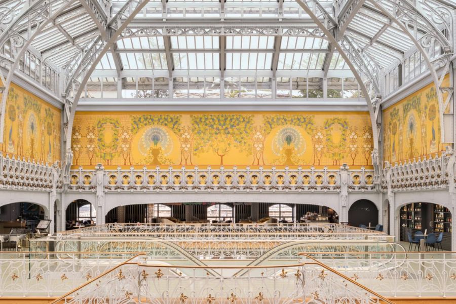 This is an image of a lovely big room with yellow accent walls and a big, high ceiling. There is a staircase in the centre leading down.